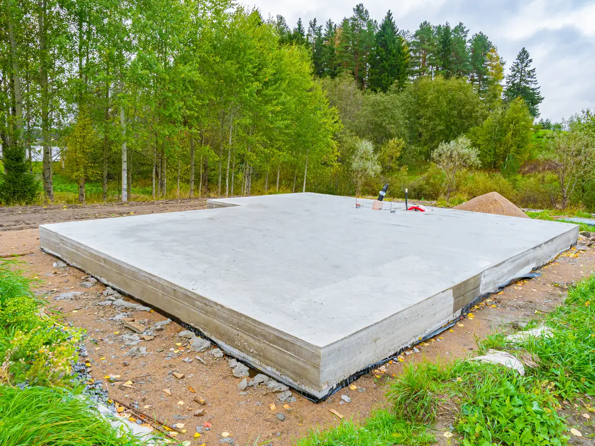 Nygjuten betongplatta på mark för husgrund i skogsmiljö